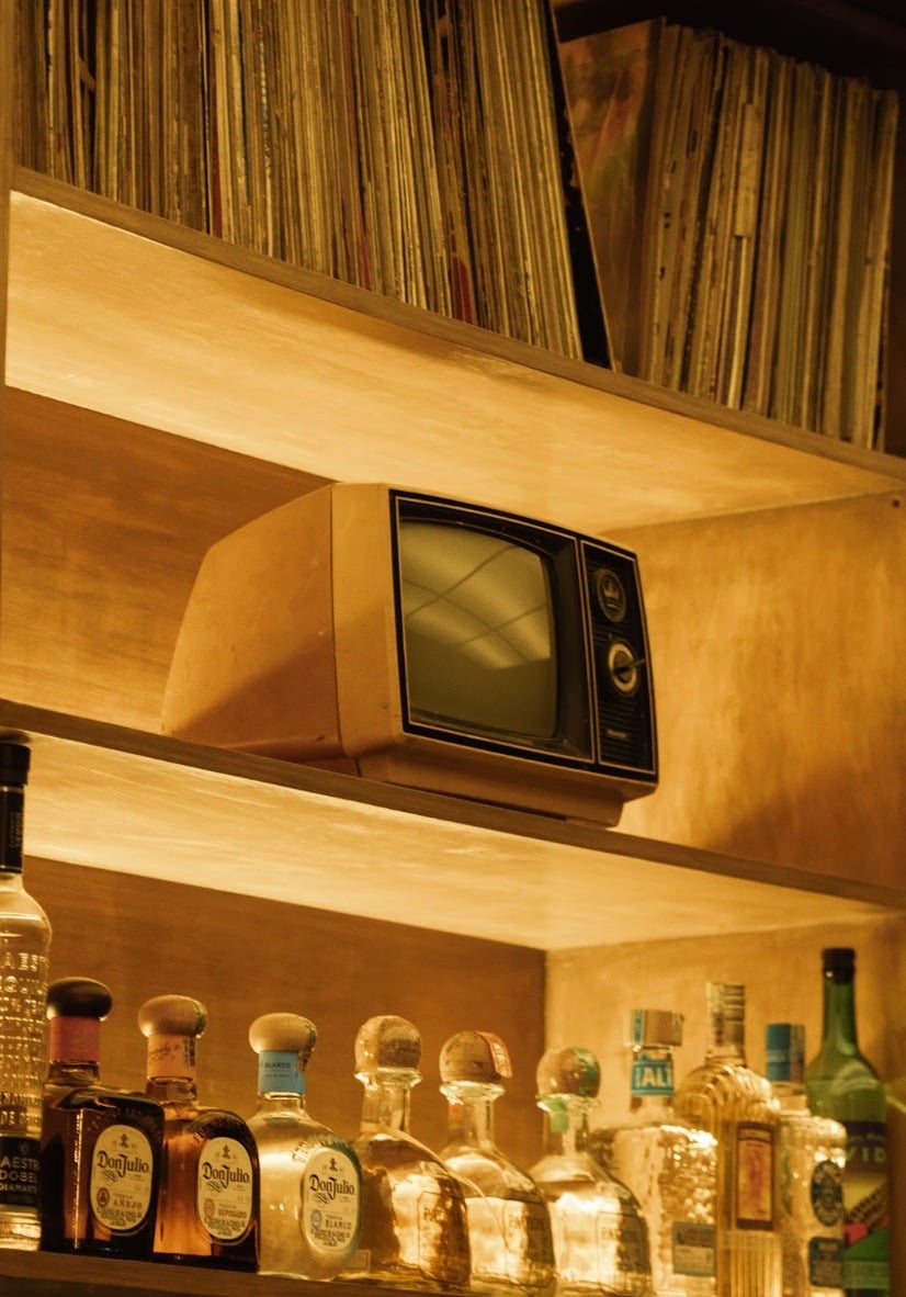 Detalle de estantes con televisor vintage, vinilos y botellas, 55DB