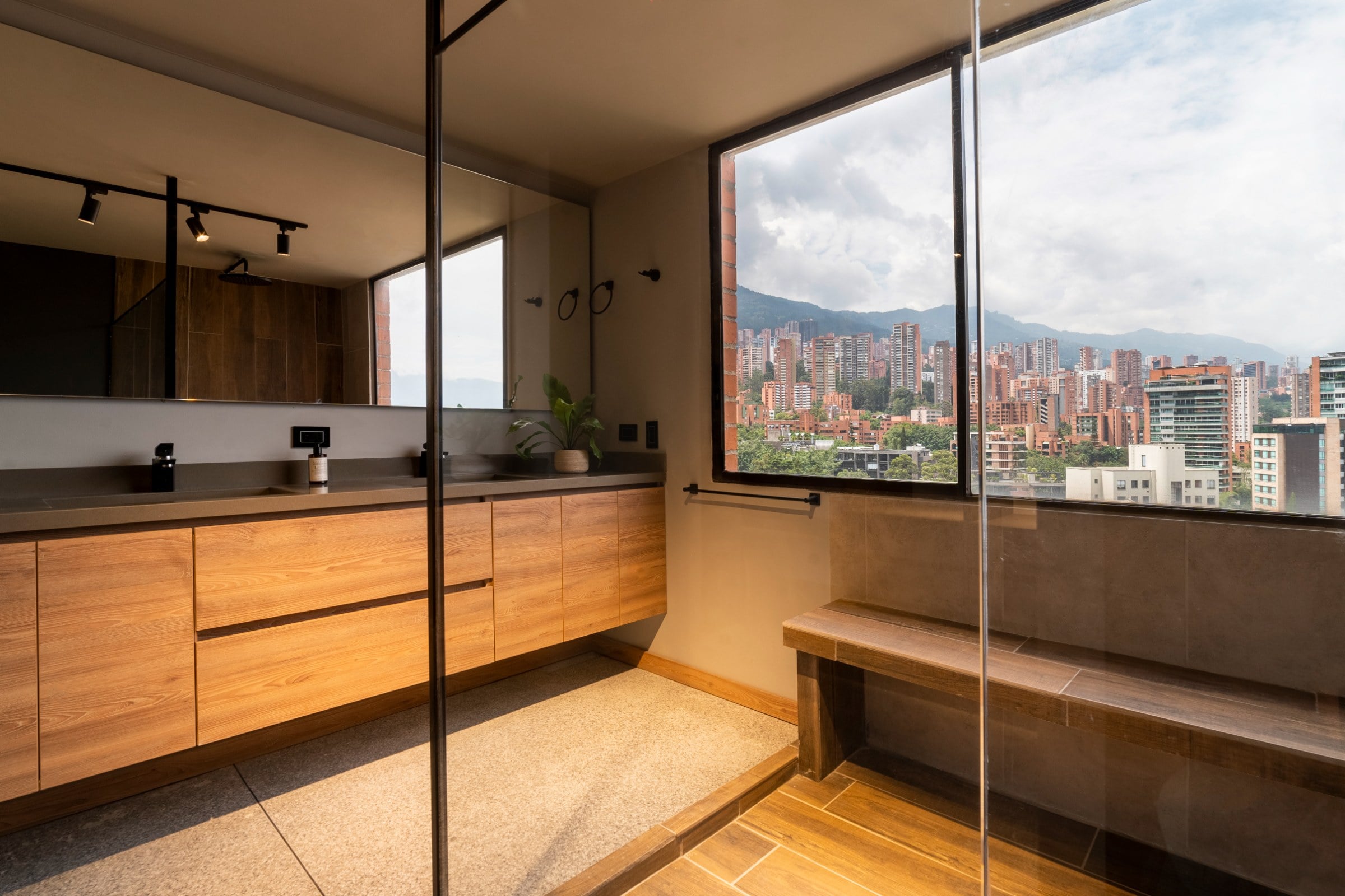 Baño con mueble en madera, mesón gris y vista a la ciudad, La Almenara