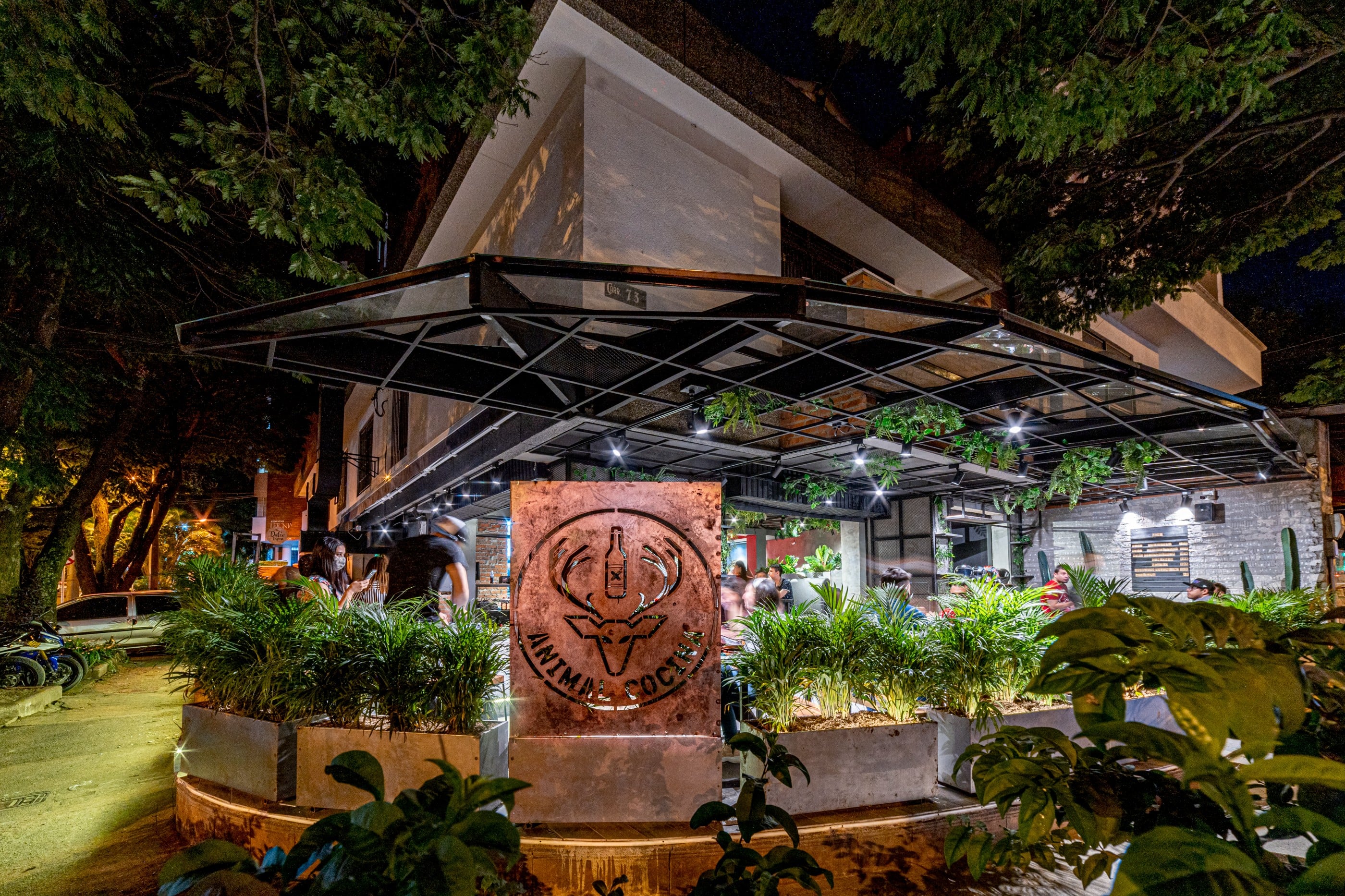 Terraza nocturna del restaurante Animal Cocina con pérgola metálica y jardines, Medellín