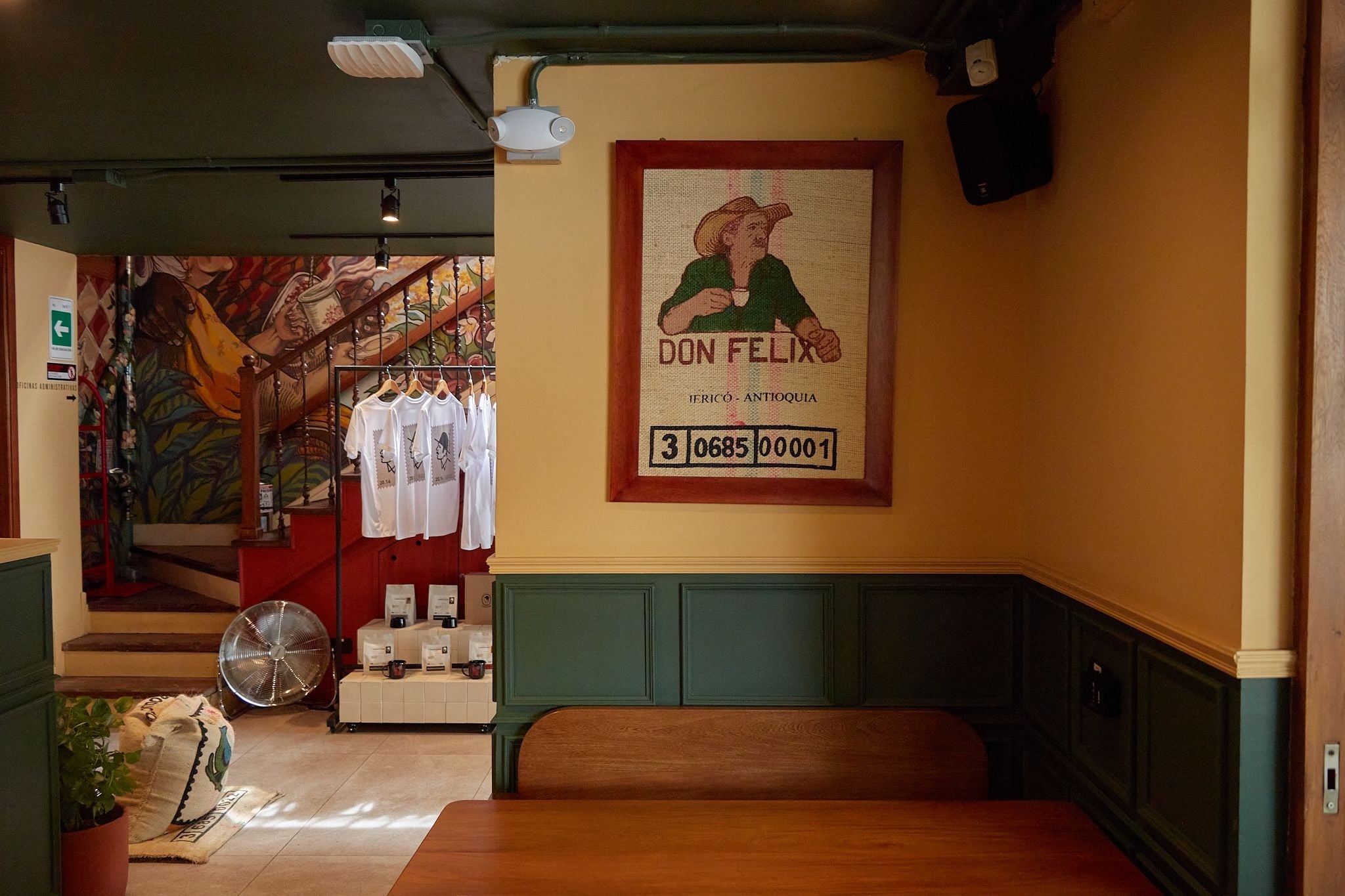 Interior de Campesino Coffee con cartel de Don Félix, mural en la escalera y banca de madera